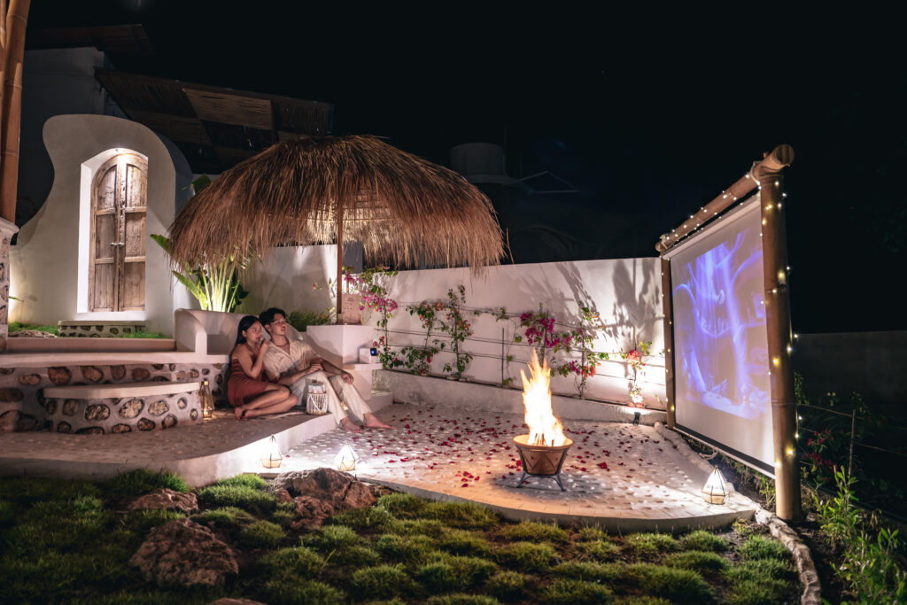 Couple enjoying a romantic evening with bonfire and outdoor movie under a bamboo hut at Camanta Penida, Nusa Penida.