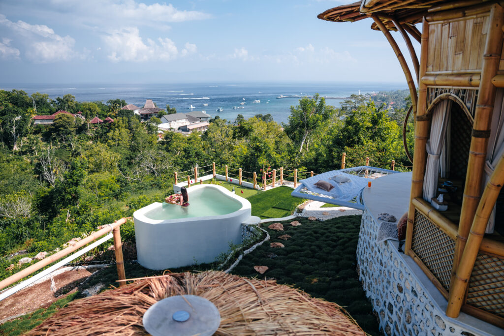 Scenic view of a woman enjoying a floating breakfast in a private plunge pool overlooking the ocean at a bamboo villa in Nusa Penida.